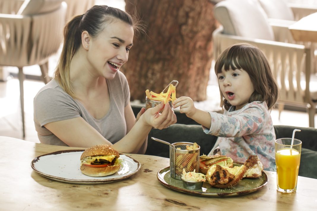 Mom with a cute daughter eating fast food in a cafe